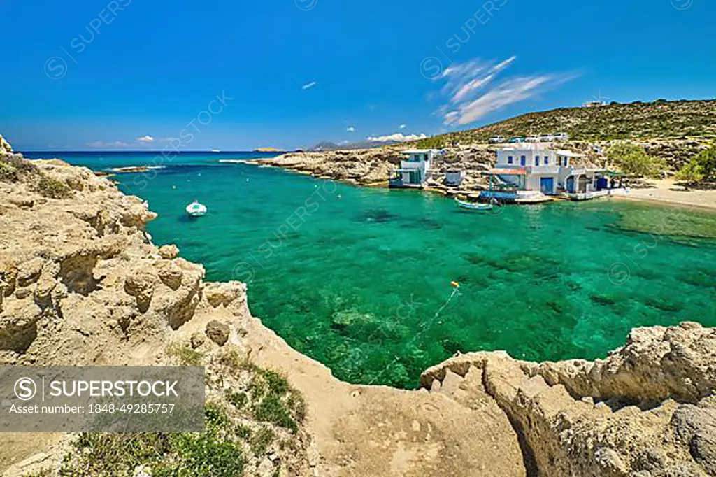 Beautiful view of secluded Mediterranean island harbour on summer day. Whitewashed houses, hills, clear blue sky, azure sea waters, beach, anchored small motor boats. Milos island, Cyclades, Greece. Mediterranean getaway vacations on remote islands