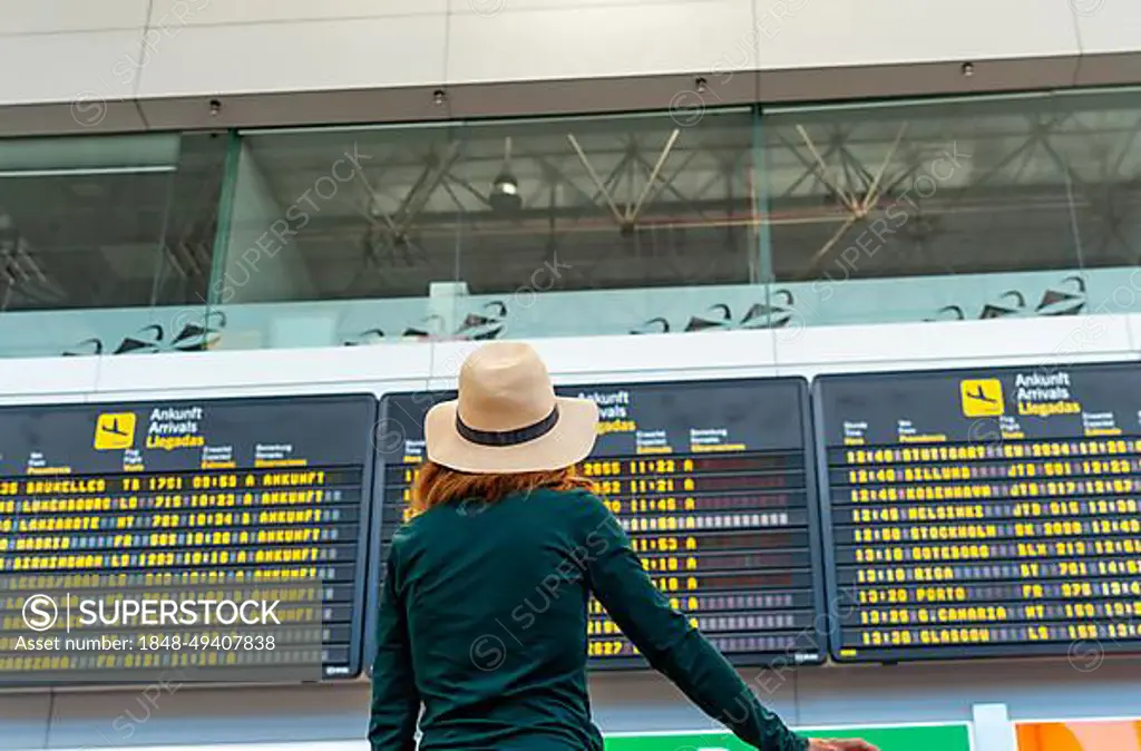 Tourist woman at the airport looking at the information on screens in the connection terminal