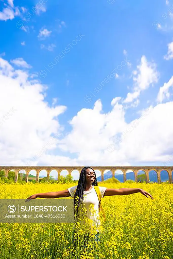 Enjoying spring on vacation, black ethnic girl with braids, traveler, in a field of yellow flowers, vertical photo