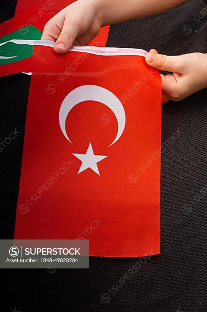 Child hand holding Turkish flag with white star and moon