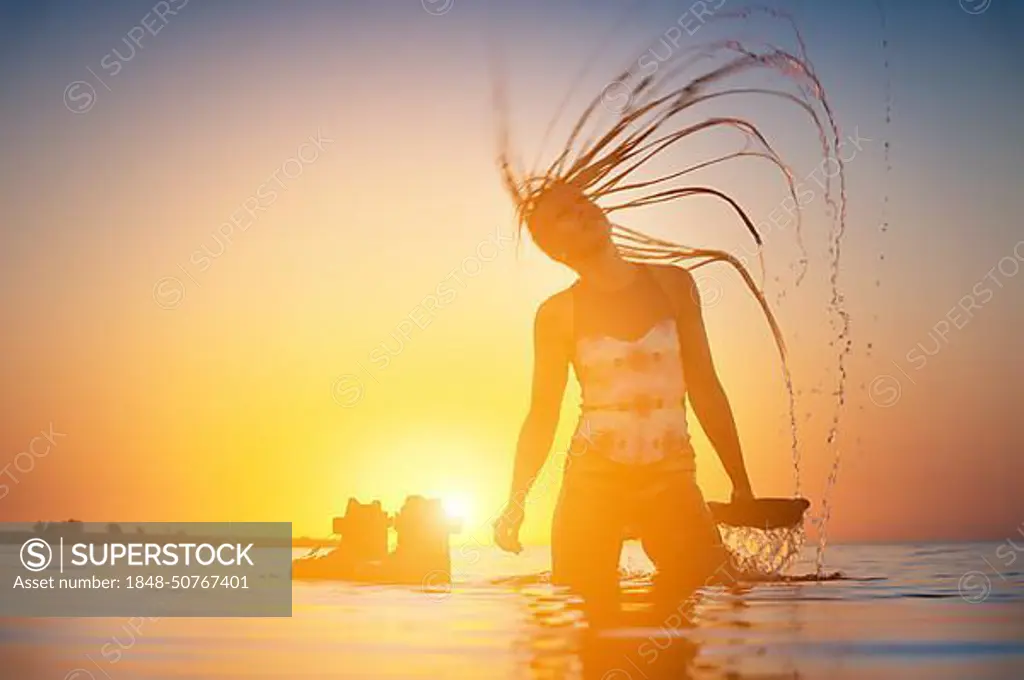 Silhouette of a slender young female athlete kite surfer swims at sunset in the sea next to her kite board