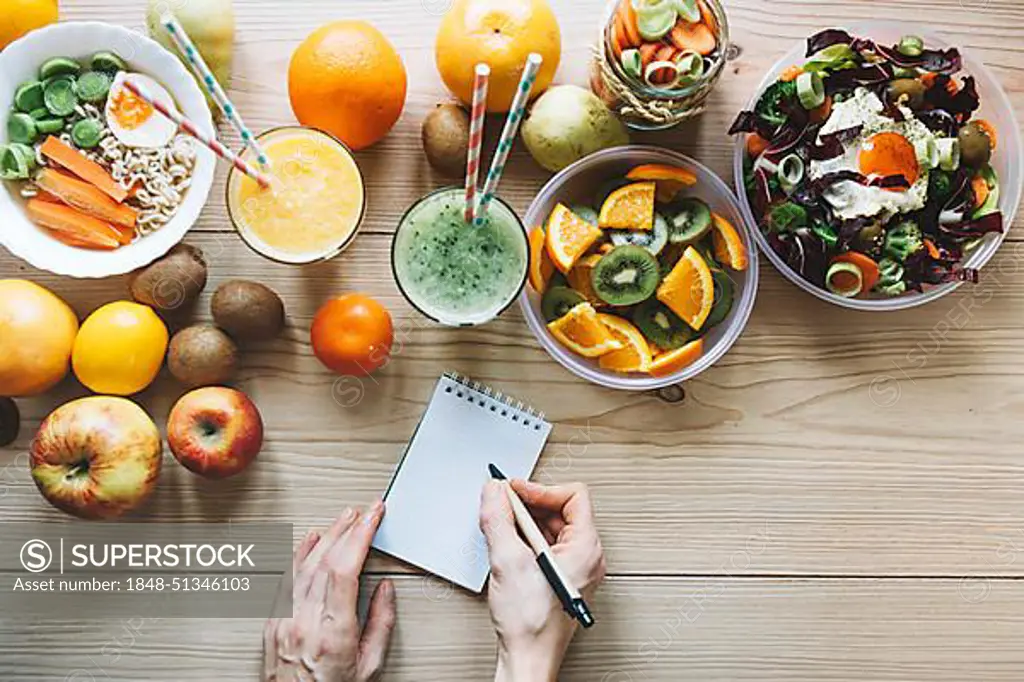 Crop hands making notes near healthy food