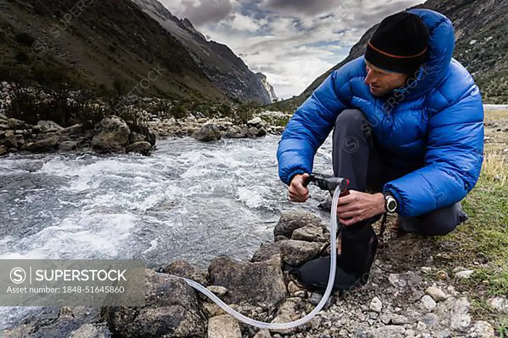 mountain climber filtering and pumping drinking water from a stream in a remote valley in the Cordillera Blanca in the Andes in Peru