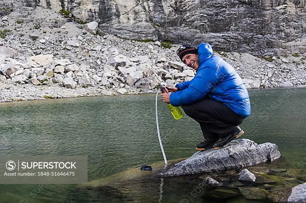 mountain climber on a rock in a lake pumping and filtering drinking water in the Andes of Peru during a climbing expedition