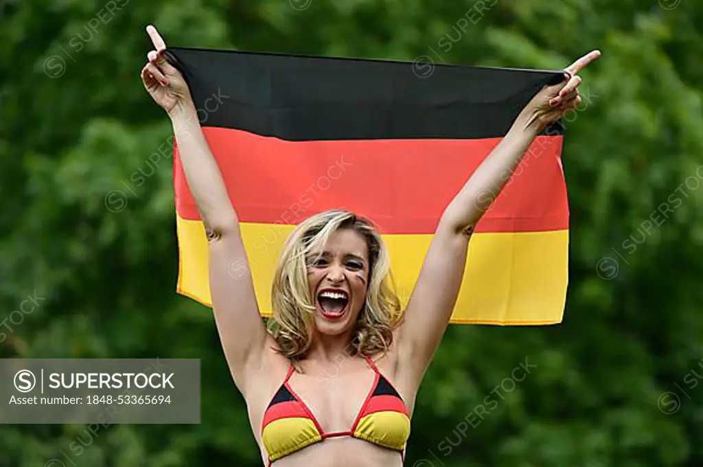 Woman in a bikini in the German national colours holding the national flag of Germany, cheering