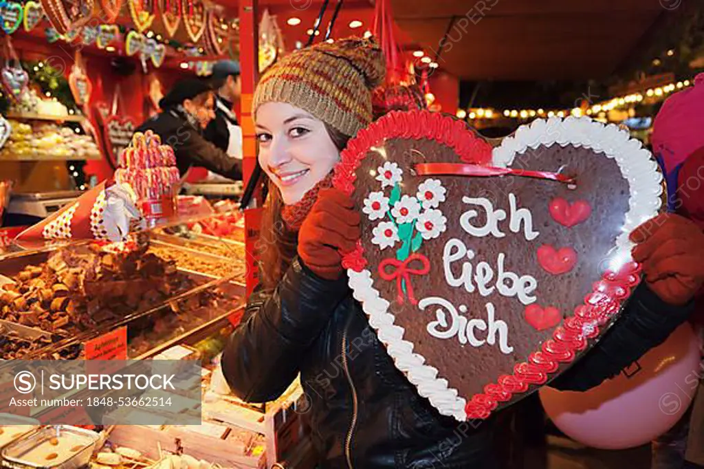 Young woman holding a Gingerbread heart with inscription "Ich liebe Dich", German for "I love you" at the Christmas market, Esslingen am Neckar, Baden-Wuerttemberg, Germany, Europe