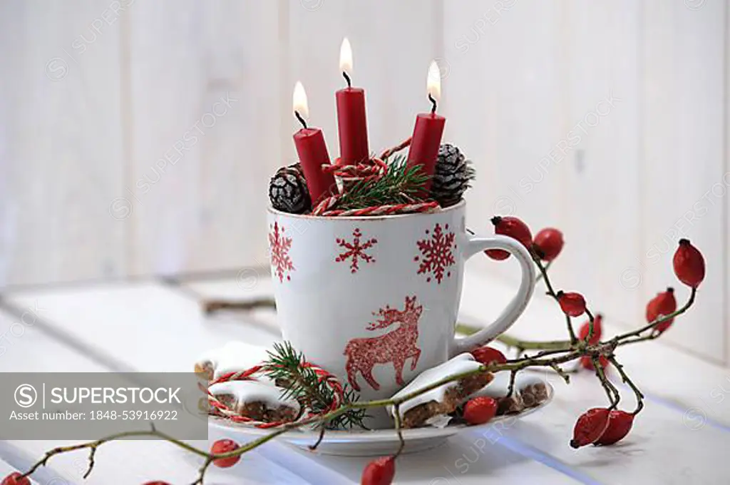 Christmas ambience with a teacup, burning candles and rose hips