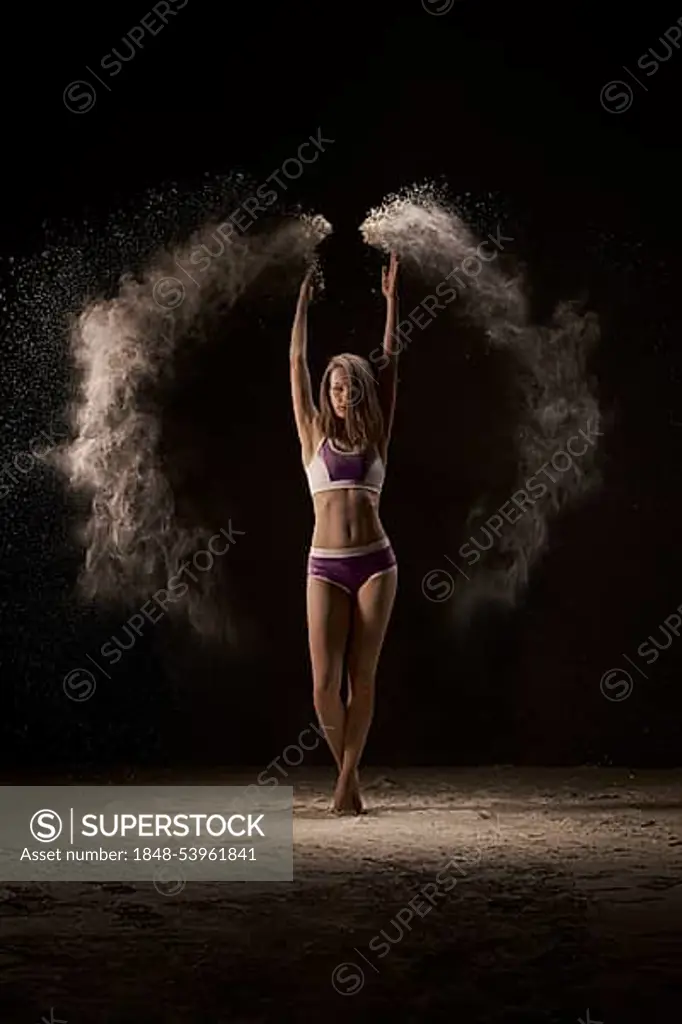 Female athlete throwing up the sports magnesia during competition in athletics against black background