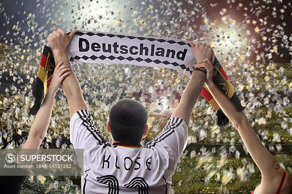 Football fan holding up a German supporters scarf, seen from behind, with confetti in a football stadium