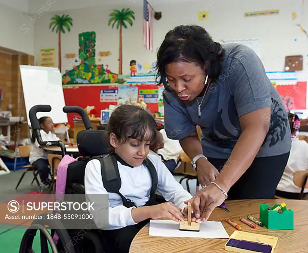 A teacher helps a girl in a wheelchair in a classroom at Oakman Elementary school; teachers and para-professionals at the school are members of the American Federation of Teachers, Detroit, Michigan, USA, North America