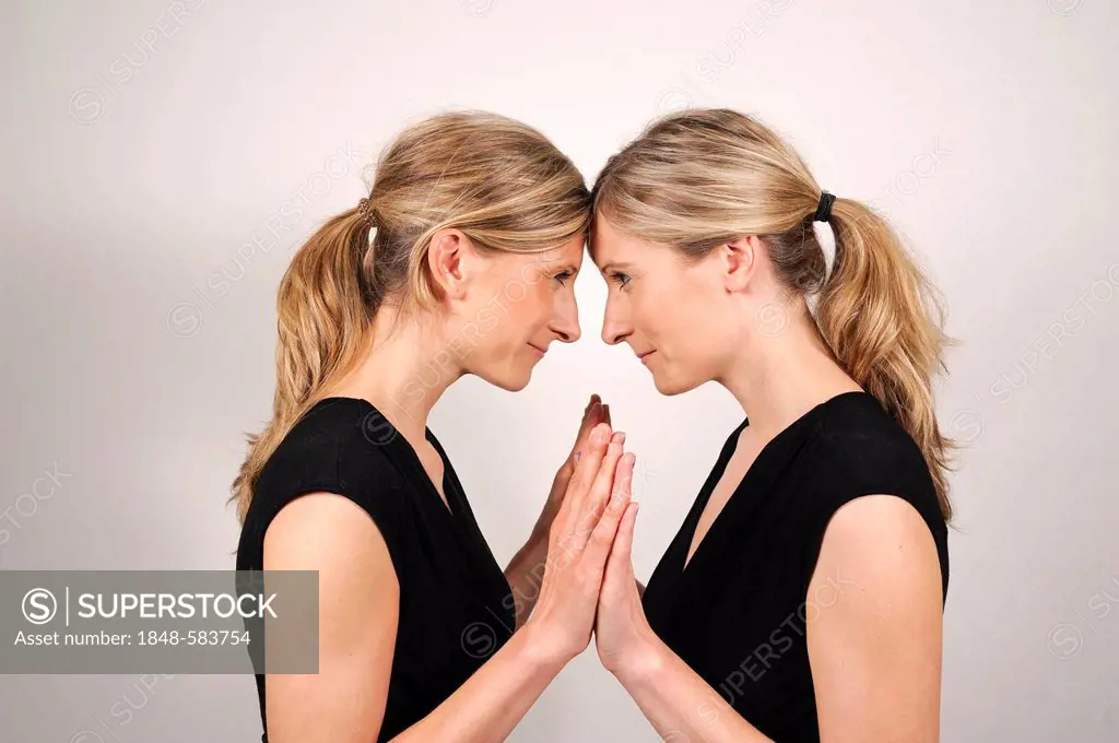 Twin sisters holding each other's hands, standing nose to nose