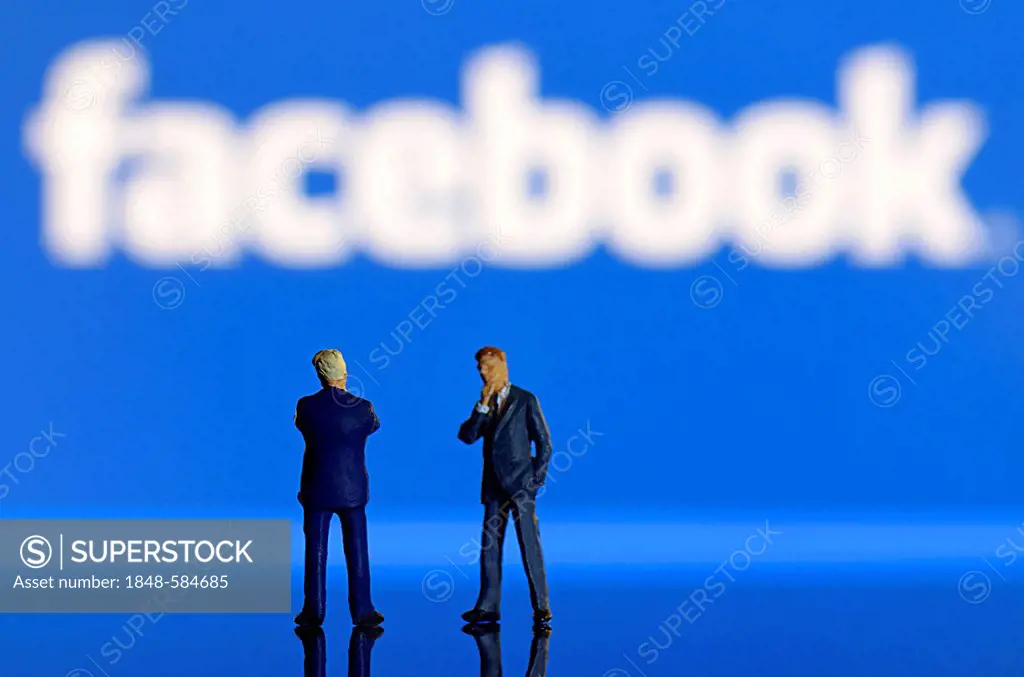 Two businessmen, miniature figures standing in front of a blurred Facebook logo, symbolic image