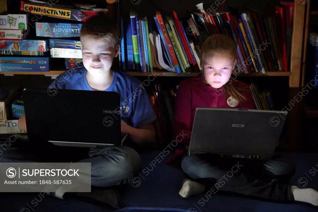 Siblings, a boy, 12 years old, and a girl, 10 years old, playing computer games on laptop computers in their room