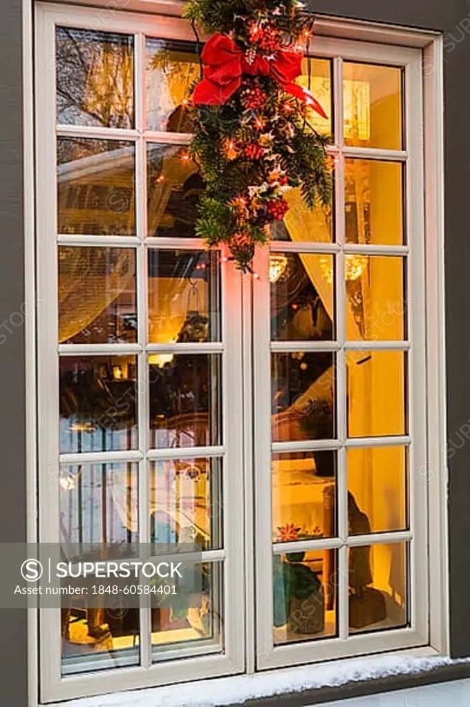 Brown and beige window with illuminated Christmas lights and decorations on an old circa 1886 white with beige and brown trim Canadiana cottage style home at dusk in winter, Quebec, Canada, North America