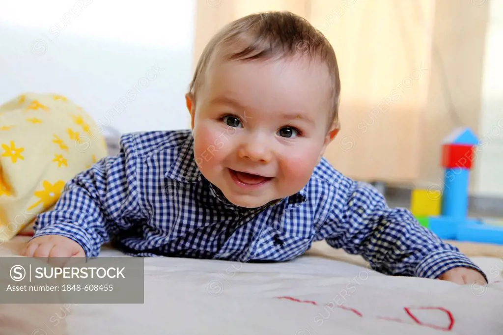 Little boy, 6 months, lying on his stomach on a blanket in his children's bedroom, smiling, Germany, Europe