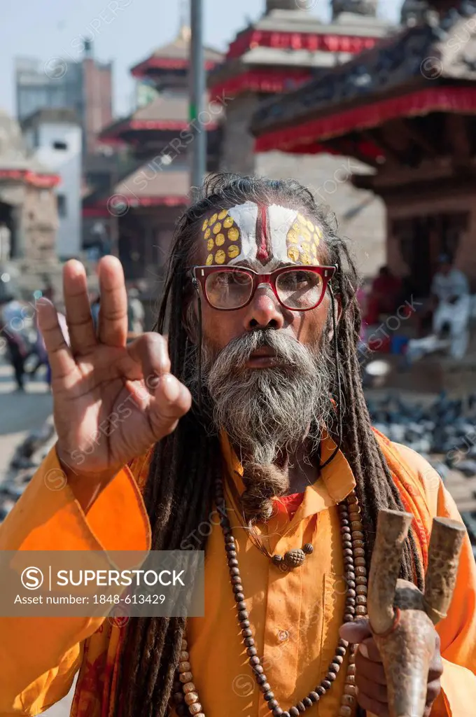 Portrait, holy man wearing glasses blessing with his hand, Mudra, Sadhu, brightly painted forehead, orange robe, beard, Hinduism, Makhan Tole Square o...