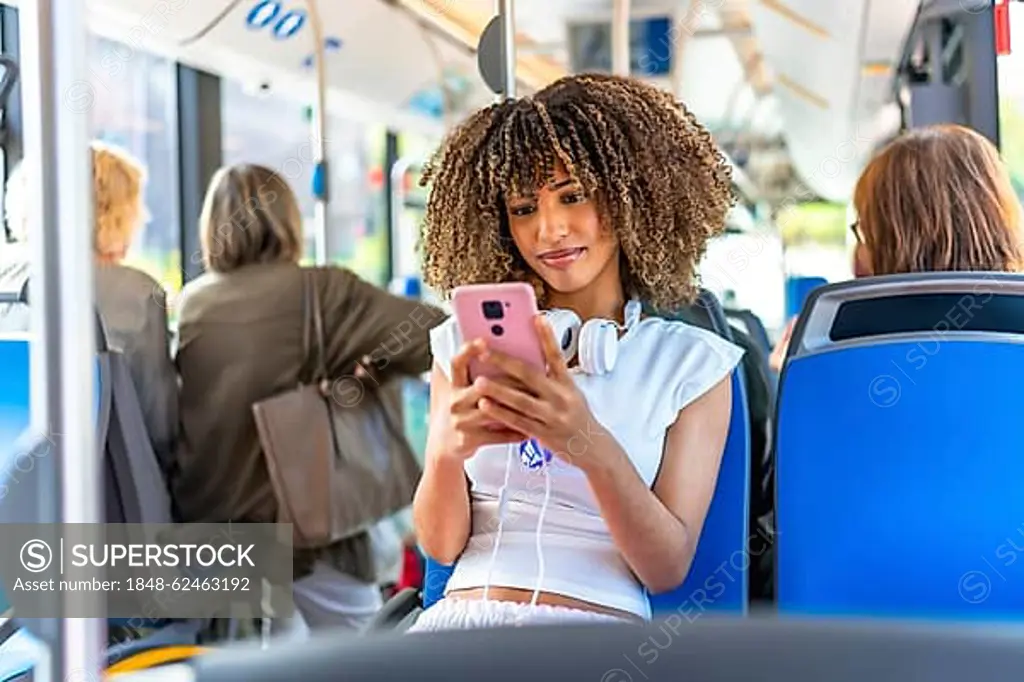 Young beauty latin woman with curly hair and casual clothes using phone distracted sitting on public bus