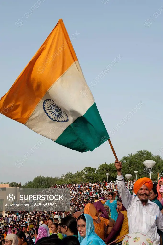 Man wearing a turban waving the Indian national flag above a crowd of people at the India Pakistan border, Punjab, India, South Asia, Asia