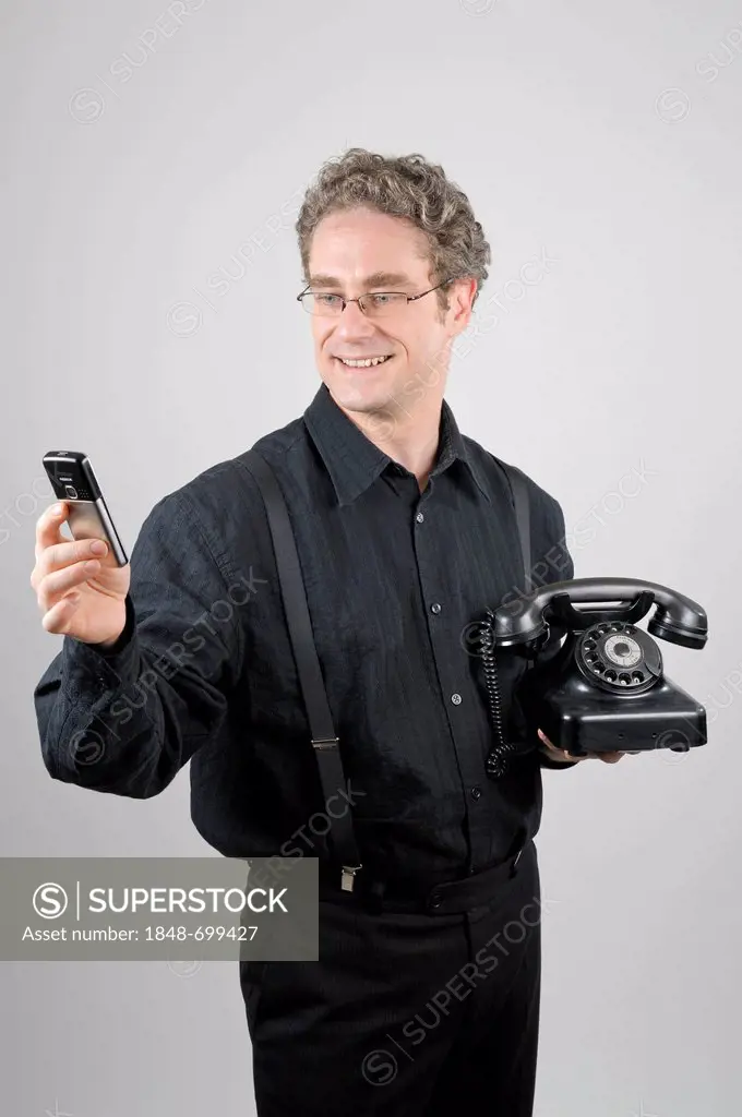 Businessman wearing a black suit holding a modern mobile phone and a historical W 38 phone