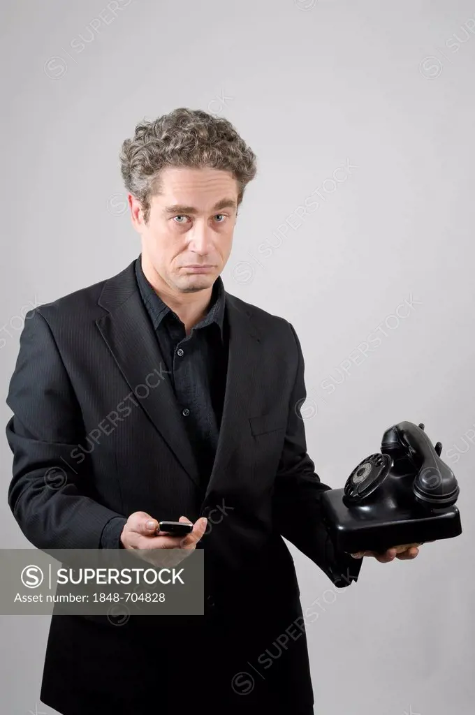 Businessman wearing a black suit holding a modern mobile phone and a historical W 38 phone