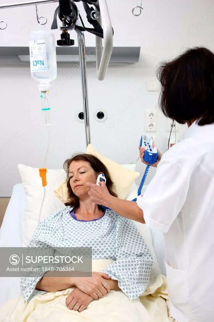 Nurse using a digital thermometer to measure the body temperature of a patient in a hospital bed