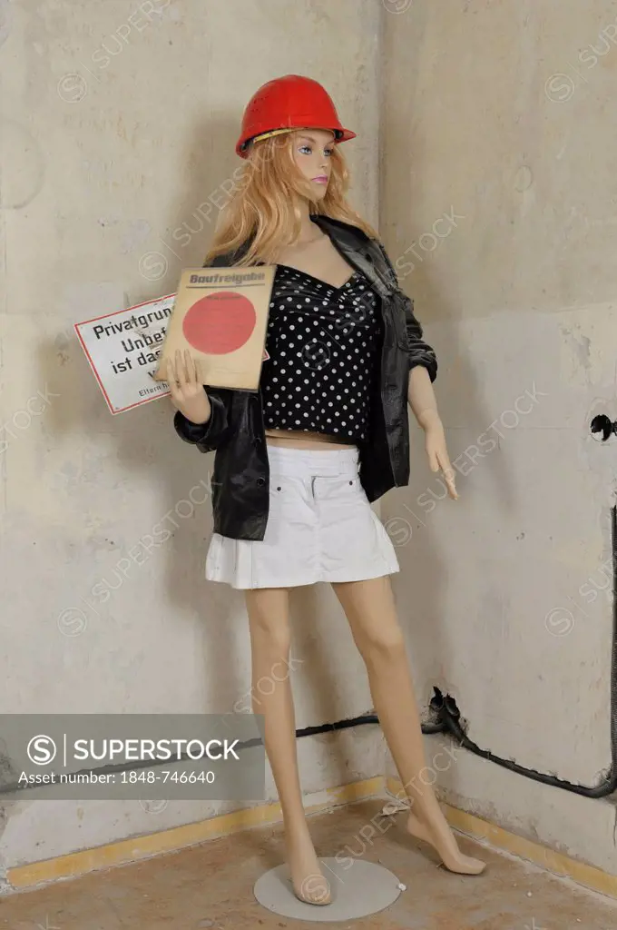 Mannequin with a hard hat on a building site, holding a construction approval and a no entry sign in her hand. Germany, Europe