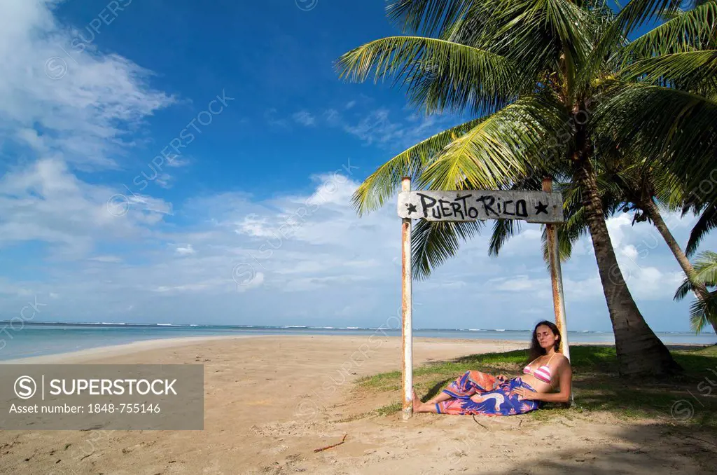 Tourist lying under a sign with the words Puerto Rico, Luquillo Beach, Puerto Rico, Caribbean