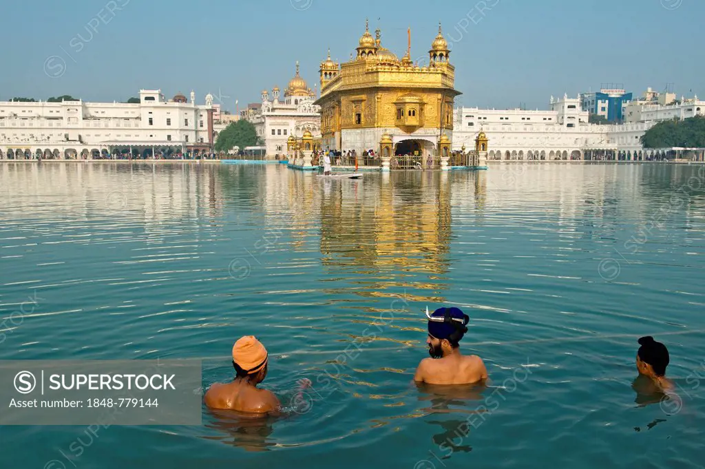 Golden Temple, Hari Mandir, the main shrine of the Sikh, three pilgrims wearing turbans taking a ritual bath in the holy lake of Amrit Sagar