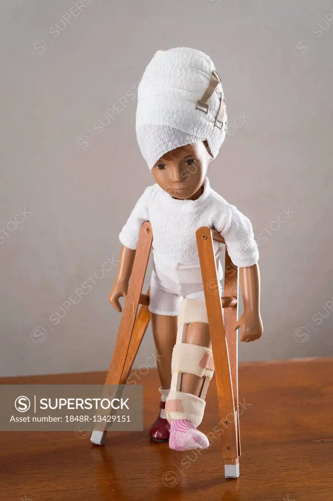 Doll with bandaged head, leg splint, crutches, walking upright, frontal view