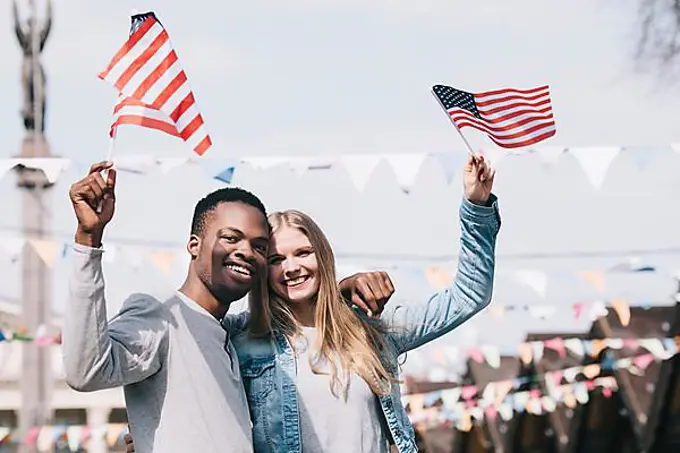 Multiethnic friends holding american flags outstretched hands