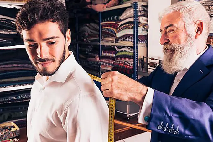 Senior male fashion designer taking measurement his customer shop