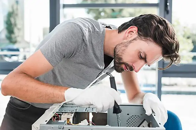 Side view young male technician working broken computer