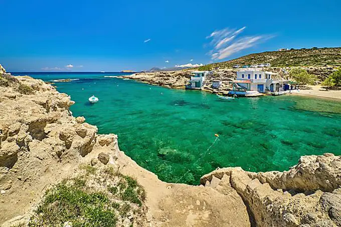 Beautiful view of secluded Mediterranean island harbour on summer day. Whitewashed houses, hills, clear blue sky, azure sea waters, beach, anchored small motor boats. Milos island, Cyclades, Greece. Mediterranean getaway vacations on remote islands