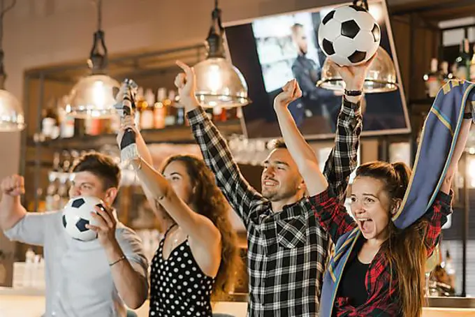 Group friends watching sport together celebrating victory bar