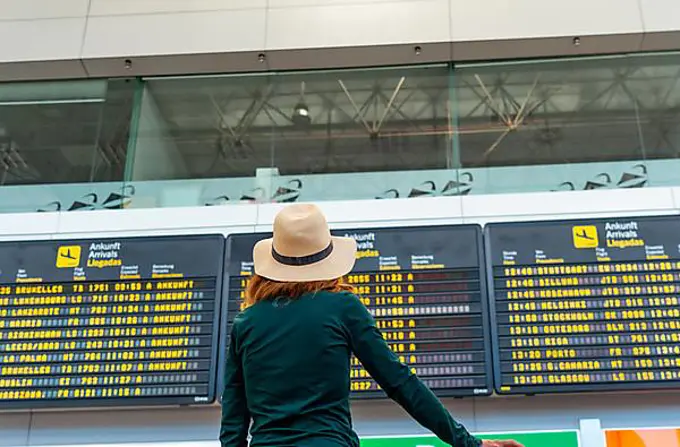 Tourist woman at the airport looking at the information on screens in the connection terminal