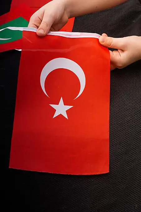 Child hand holding Turkish flag with white star and moon