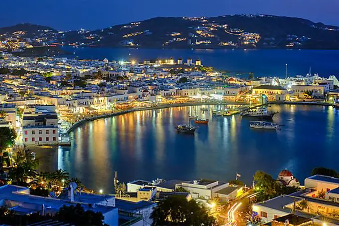 View of Mykonos town Greek tourist holiday vacation destination with famous windmills, and port with boats and yachts illuminated in the evening blue hour, Mykonos, Cyclades islands, Greece, Europe