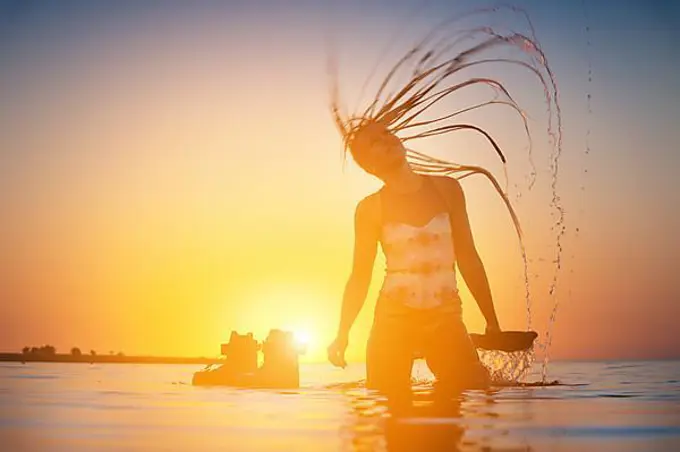 Silhouette of a slender young female athlete kite surfer swims at sunset in the sea next to her kite board