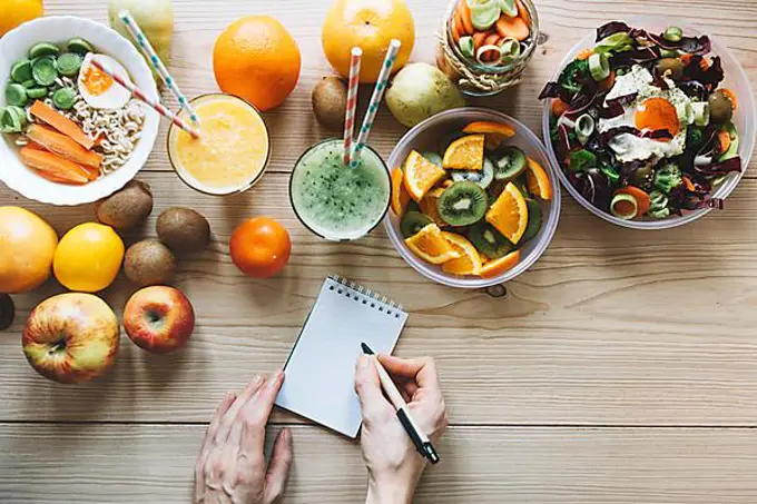 Crop hands making notes near healthy food