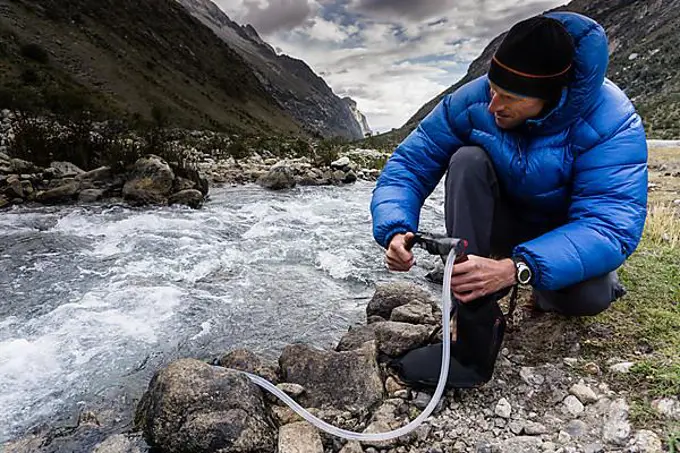 mountain climber filtering and pumping drinking water from a stream in a remote valley in the Cordillera Blanca in the Andes in Peru