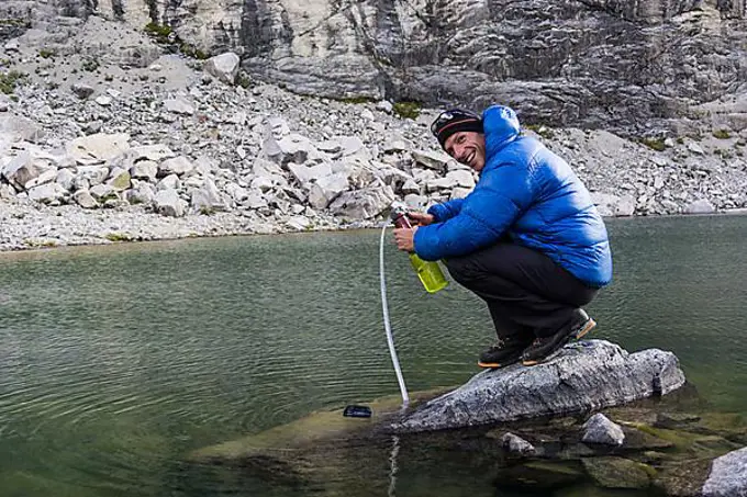 mountain climber on a rock in a lake pumping and filtering drinking water in the Andes of Peru during a climbing expedition