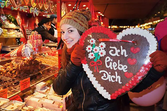 Young woman holding a Gingerbread heart with inscription "Ich liebe Dich", German for "I love you" at the Christmas market, Esslingen am Neckar, Baden-Wuerttemberg, Germany, Europe