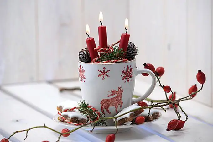 Christmas ambience with a teacup, burning candles and rose hips