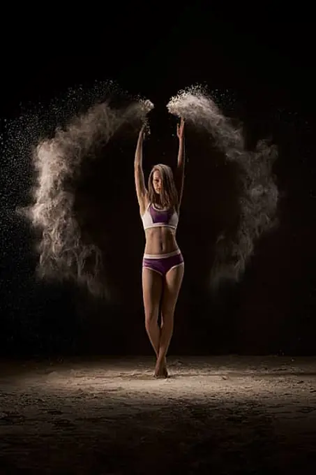 Female athlete throwing up the sports magnesia during competition in athletics against black background