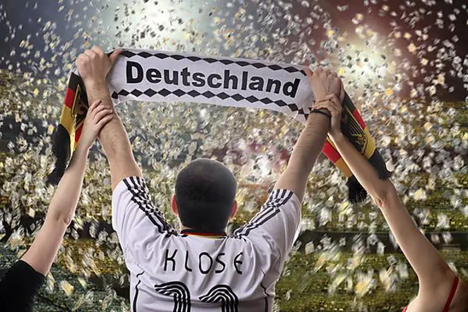 Football fan holding up a German supporters scarf, seen from behind, with confetti in a football stadium