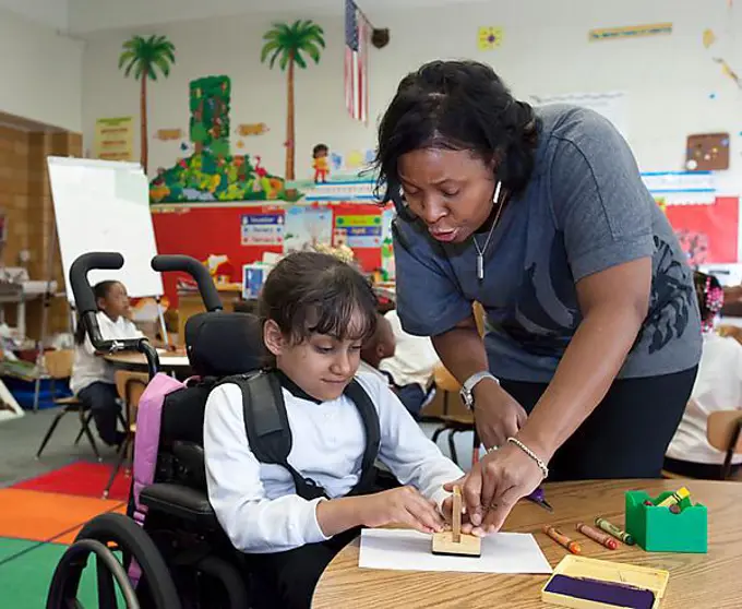 A teacher helps a girl in a wheelchair in a classroom at Oakman Elementary school; teachers and para-professionals at the school are members of the American Federation of Teachers, Detroit, Michigan, USA, North America