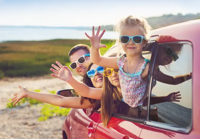 Portrait of a smiling family with two children at beach in the car. Holiday and travel concept