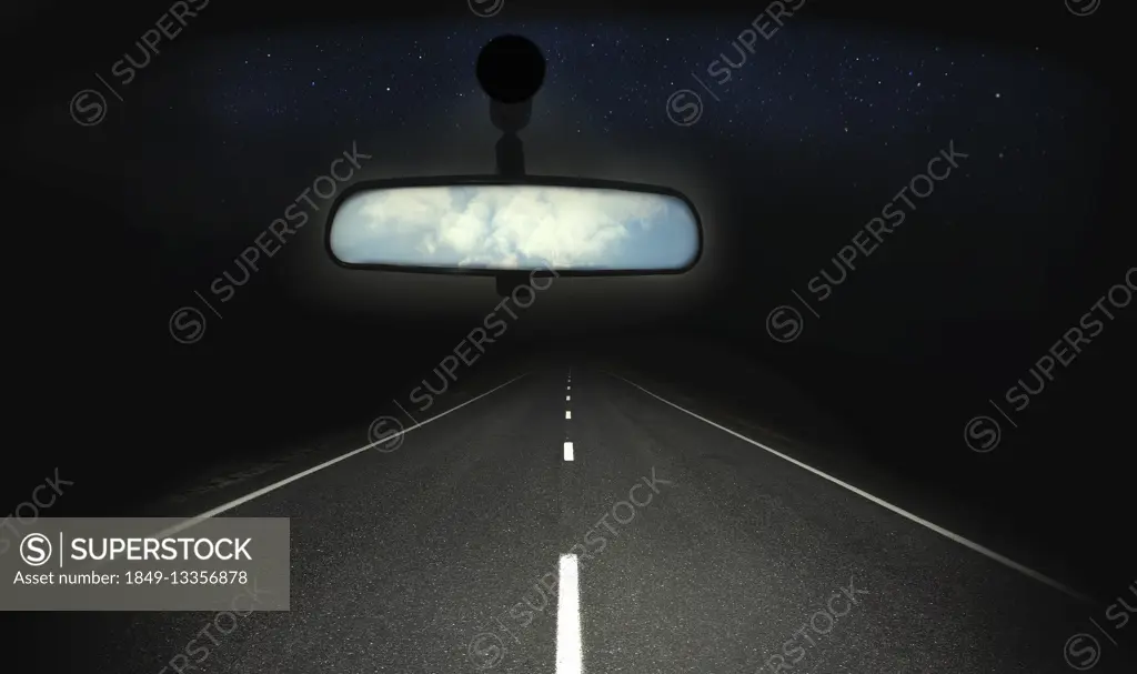 Blue sky in rear view mirror of car with dark straight road ahead