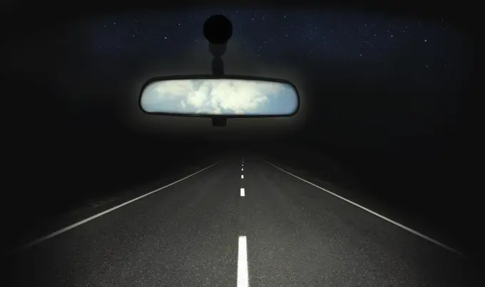 Blue sky in rear view mirror of car with dark straight road ahead