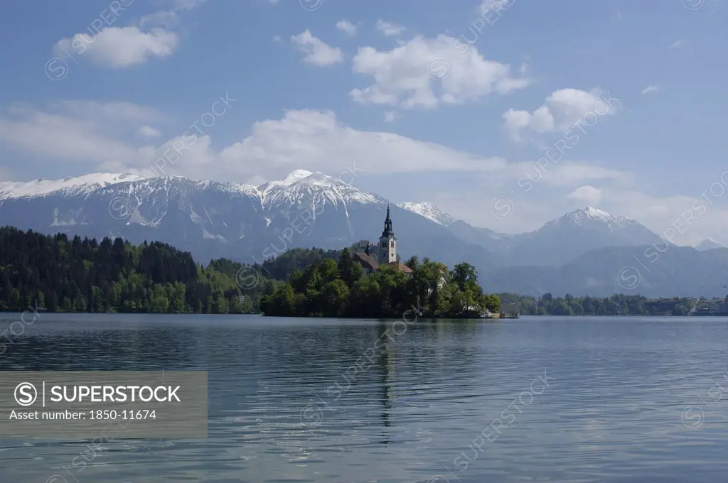 Slovenia, Lake Bled, View Over The Lake Toward Bled Island And Tower Of The Church Of The Assumption With Snow Capped Peaks Of The Julian Alps Behind